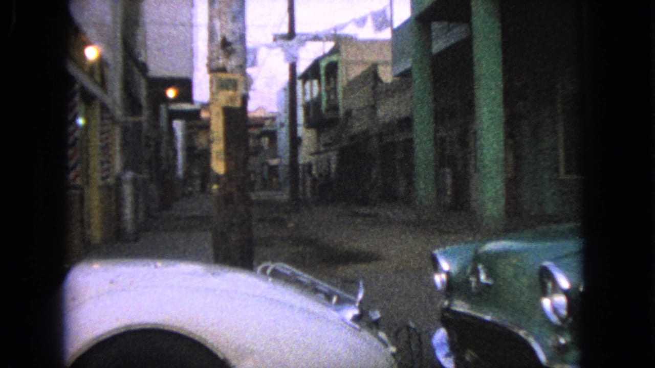 1963 Barrington, Illinois street view with classic cars, narrow storefronts, overhead laundry, and a barber pole partly visible.