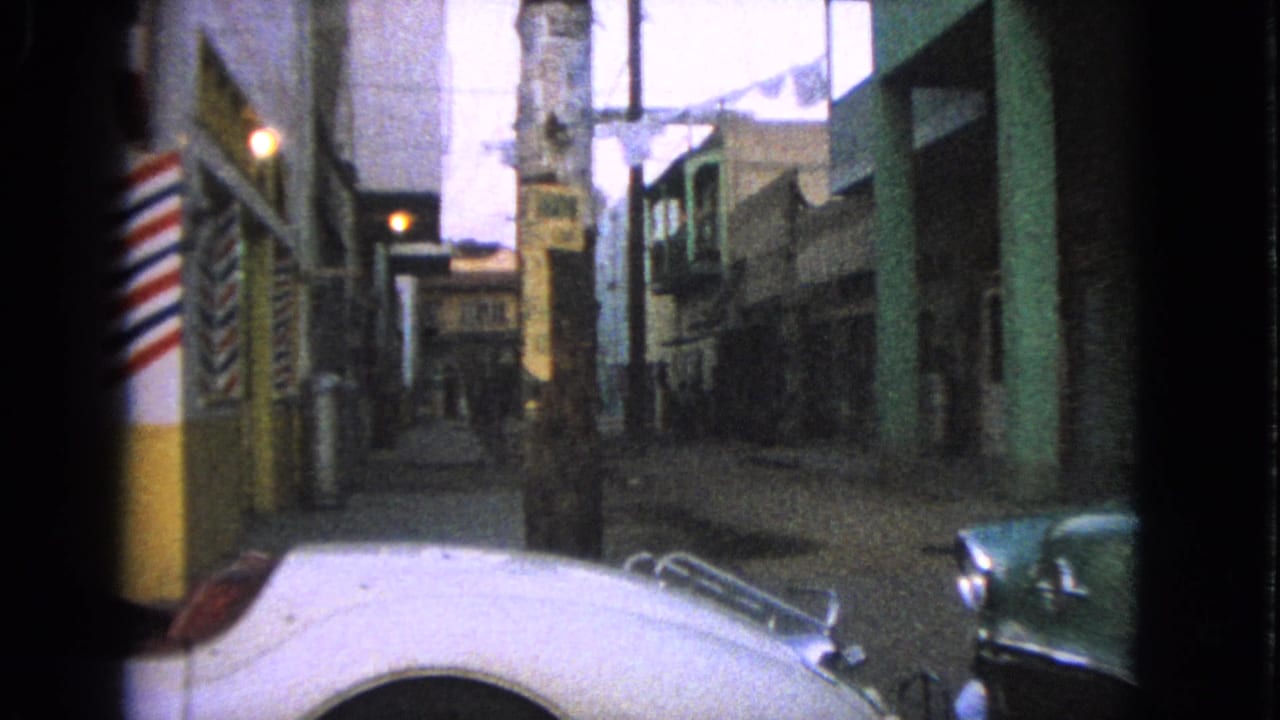 Barrington street scene from 1963 with a white car hood, green sedan, barber pole, storefront facades, and laundry strung above the lane.
