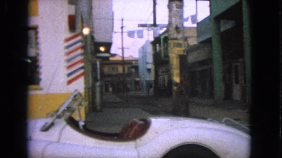 1963 Barrington view passing a barber shop pole and white convertible, with storefronts, utility poles, and laundry lines visible down the street.