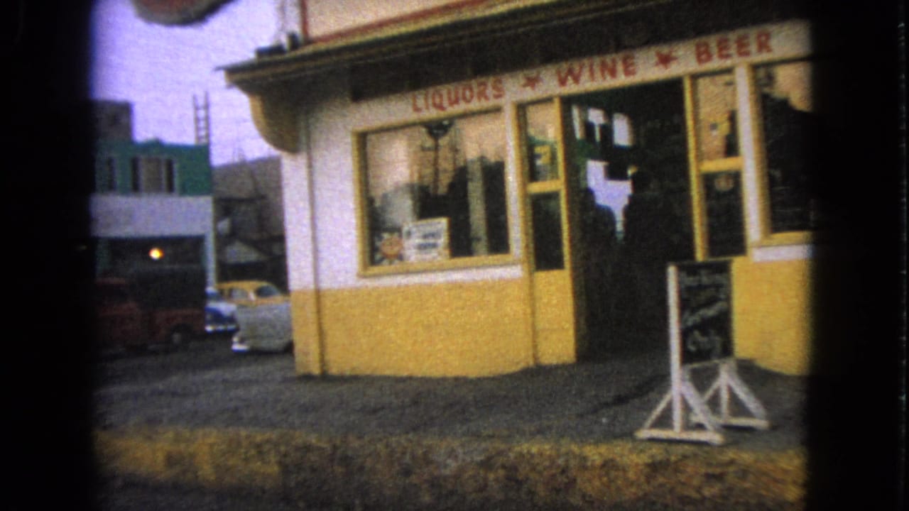Barrington, Illinois storefront view showing a liquor store corner, visible LIQUORS WINE BEER sign, sidewalk board, and mid-century cars in the background.