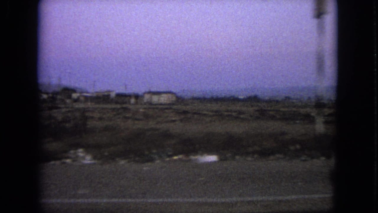 1963 8mm roadside view in the Barrington, Illinois metadata context, showing sparse land, low buildings, poles, and a hazy sky.