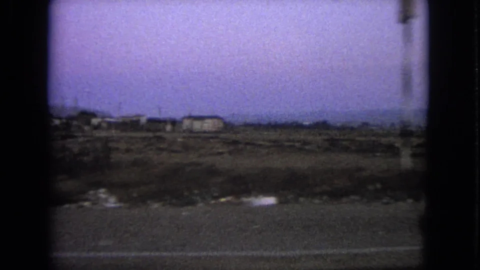 1963 8mm roadside view in the Barrington, Illinois metadata context, showing sparse land, low buildings, poles, and a hazy sky.