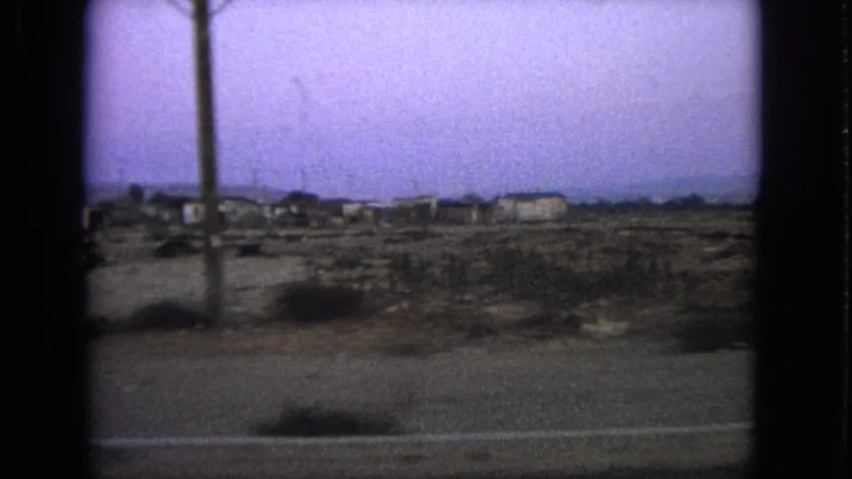 Barrington-context 1963 home-movie frame with a foreground utility pole, sparse roadside land, distant buildings, and soft 8mm color shift.