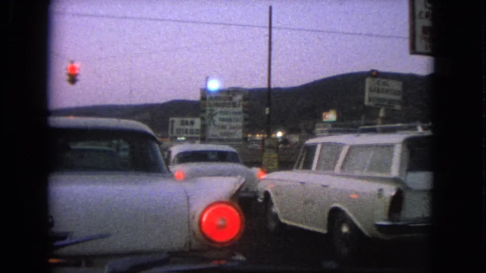1963 Barrington, Illinois traffic scene showing a classic car rear, a white station wagon, red signal, and roadside signs.