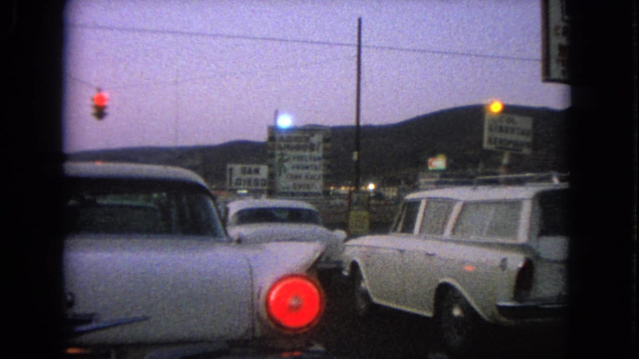 1963 Barrington, Illinois drive-in lot with parked period cars, a white station wagon, signs, and a red taillight in twilight.