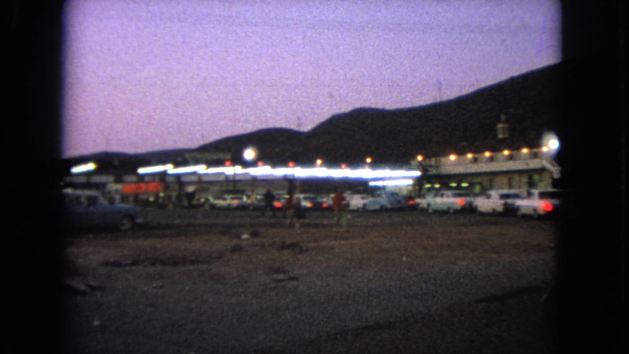 Similar dusk view of cars parked near a brightly lit low building.