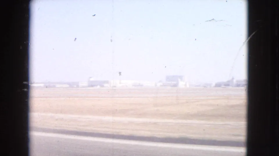 Bright overexposed 8mm frame from the Barrington clip showing an open lot and distant low structures.