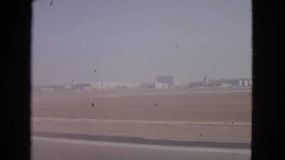 A moving 8mm view of Barrington airport grounds in 1963, with distant hangar-like buildings and a broad runway area.