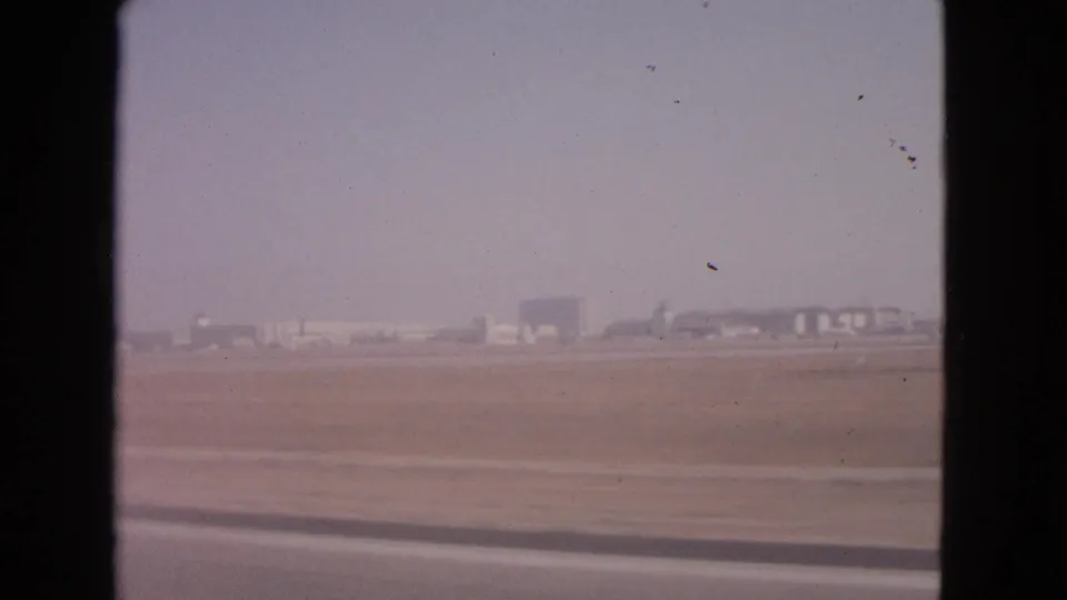 Barrington, Illinois airport buildings appear across a flat field in this faded 1963 8mm frame from a moving vantage point.