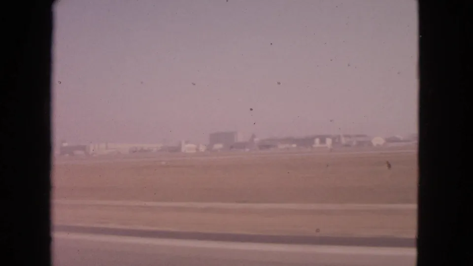 Warm faded 8mm view of a 1963 Barrington airport field, with runway pavement in front and distant structures near the horizon.