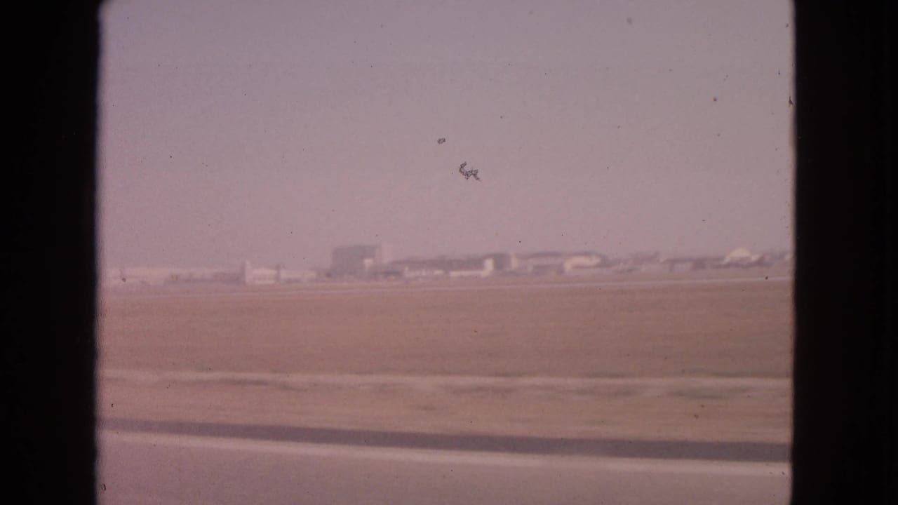 Open flat terrain with distant buildings, framed by dark vertical car-window edges.