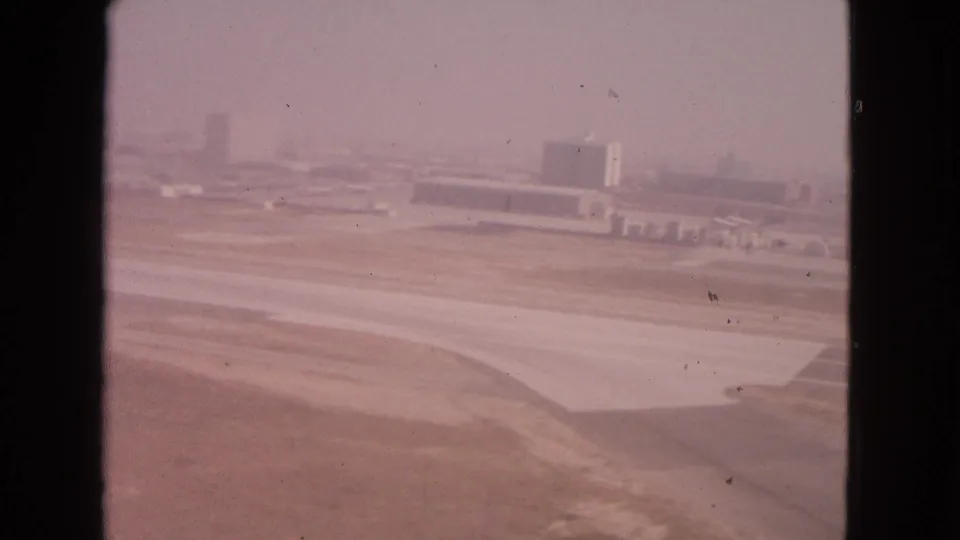 1963 Barrington, Illinois airport view across runway and apron pavement toward low buildings under a hazy sky.