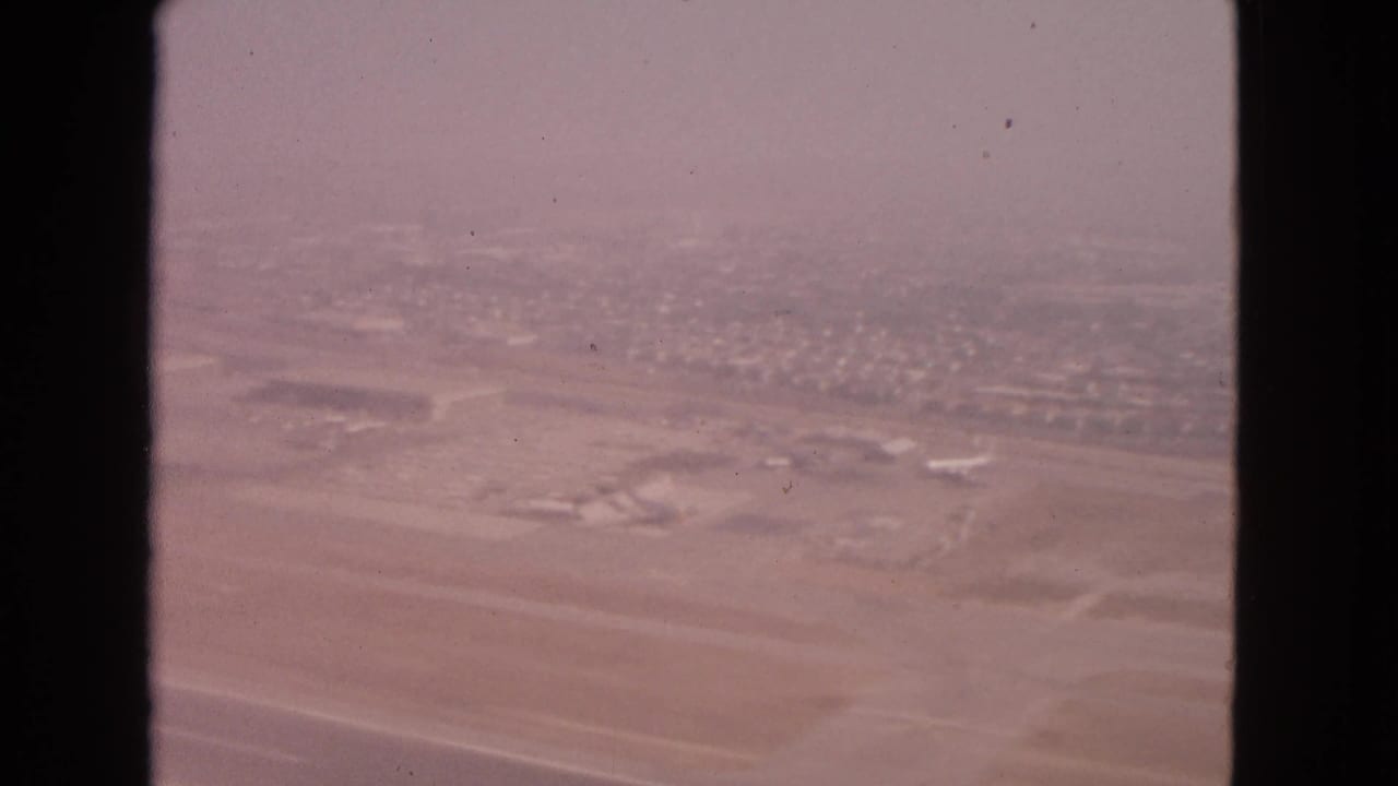 Hazy aerial view of airport runways, parked aircraft, and distant suburban homes.