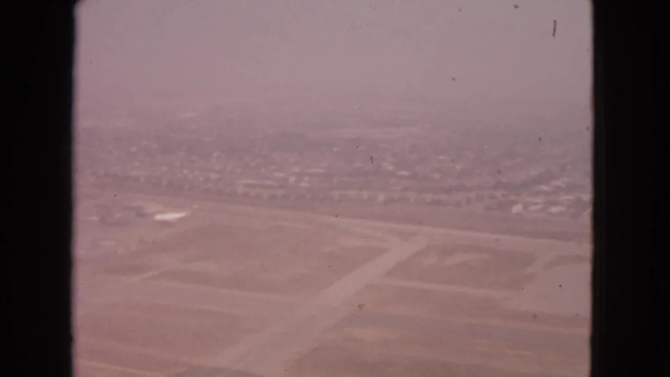 Aerial 8mm frame from 1963 Barrington, Illinois, with runway geometry, airport field areas, and suburban homes under haze.