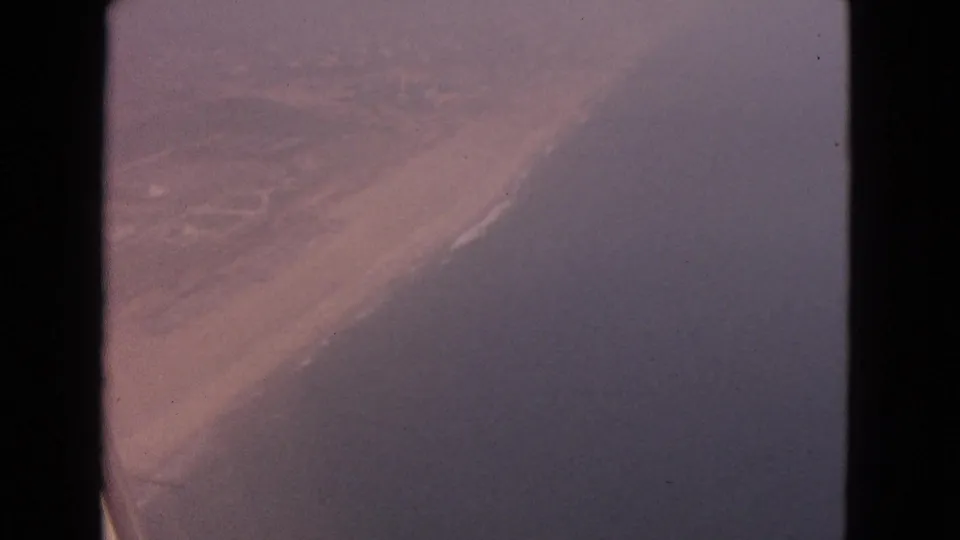Aerial 8mm frame from 1963 showing a muted shoreline and water through a dark vertical edge in the scanned frame.