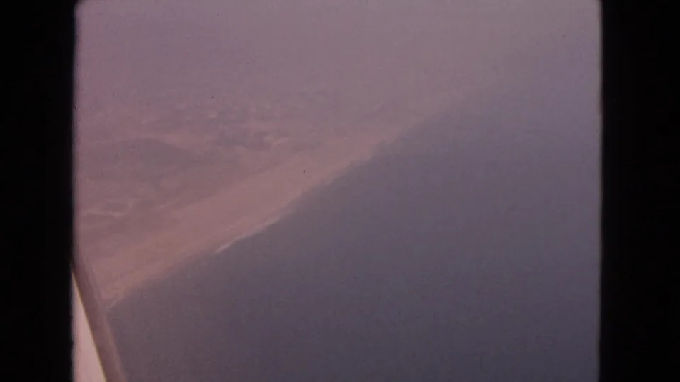 1963 8mm airplane-window view labeled Barrington, Illinois, showing haze, a dark aircraft edge, and indistinct land or water below.