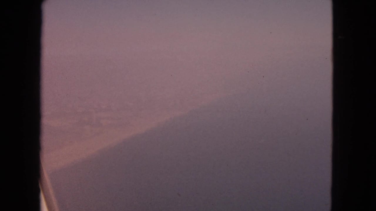 Soft aerial view of snow-covered ground and pale sky through an airplane window.