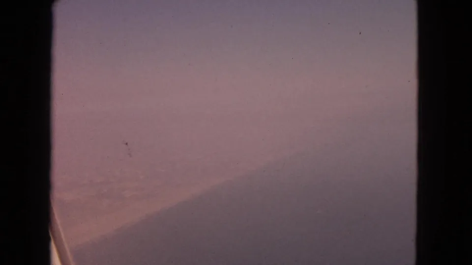 Blurred 8mm winter aerial view from an airplane window, with snow below and a faint wing edge in the lower frame.
