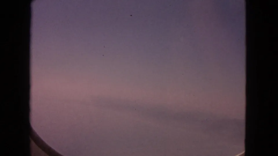1963 8mm airplane-window shot over a hazy winter landscape near Barrington, with muted pink and purple tones.