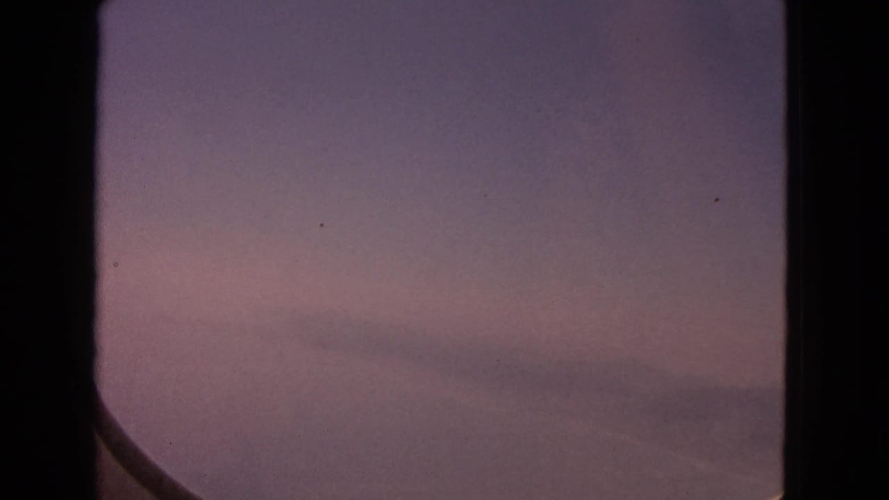 1963 8mm home-movie view from an airplane window, showing a pink sunset sky with faint clouds and a dark window edge.