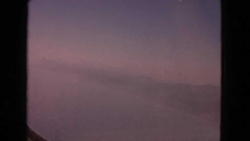 End frame of the 1963 8mm clip, with a pink-lavender sky, faint cloud forms, and the aircraft window framing the view.