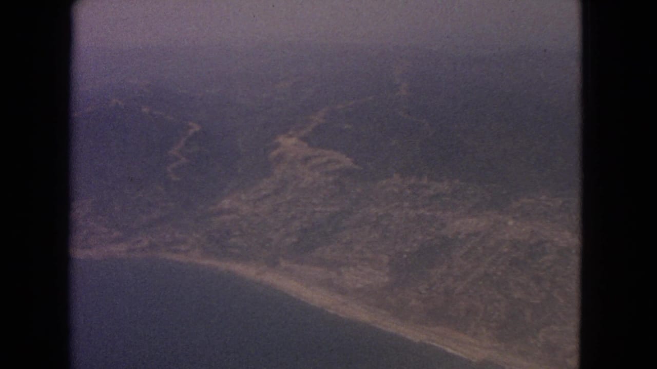 Aerial view of a hazy coastline and inland hills framed by dark film borders.