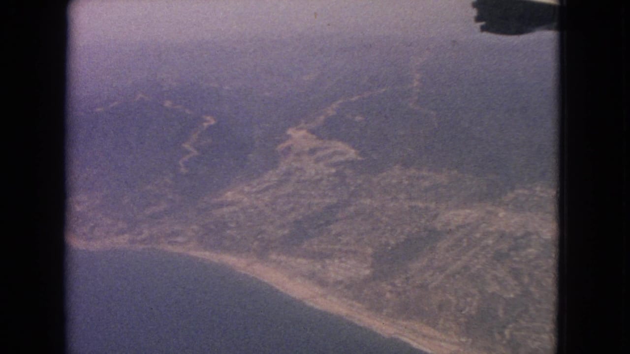Aerial view of shoreline, hills, and water seen through dark film-frame edges.