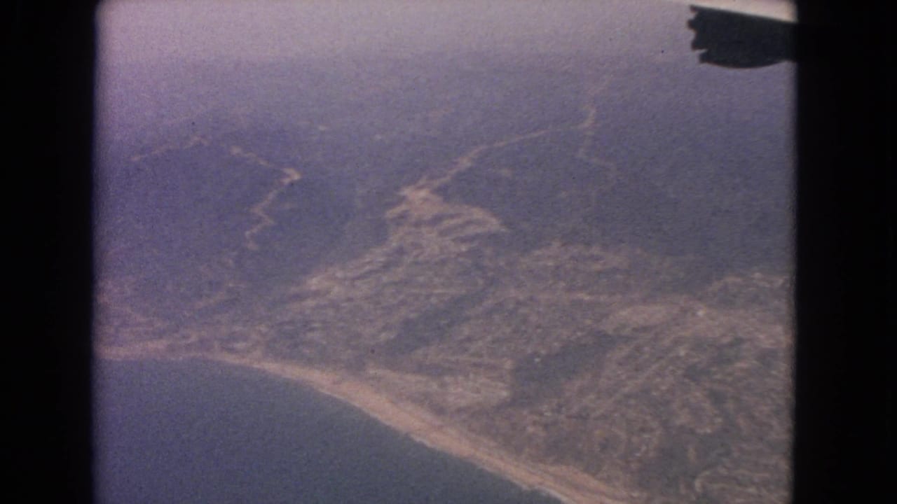 Coastal terrain and water below, with a dark airplane or film edge at upper right.