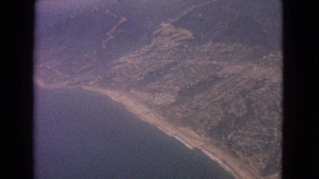 Aerial view of coastline, ocean, hills, and dark airplane-window framing.
