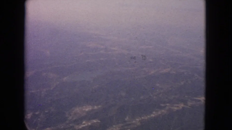 1963 8mm view from an airplane window over hazy terrain near Barrington, Illinois, with the aircraft window edge framing the scene.