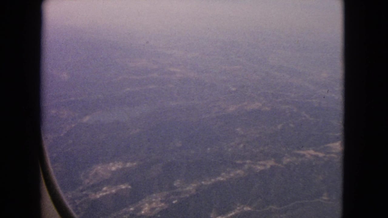 A 1963 passenger view through an aircraft window, looking down at muted hills, fields, and developed patches near Barrington, Illinois.