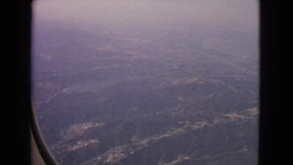 A 1963 passenger view through an aircraft window, looking down at muted hills, fields, and developed patches near Barrington, Illinois.