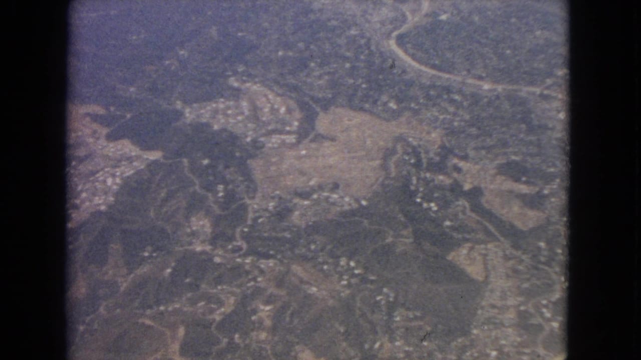Aerial view of roads, fields, wooded areas, and scattered buildings below a plane.