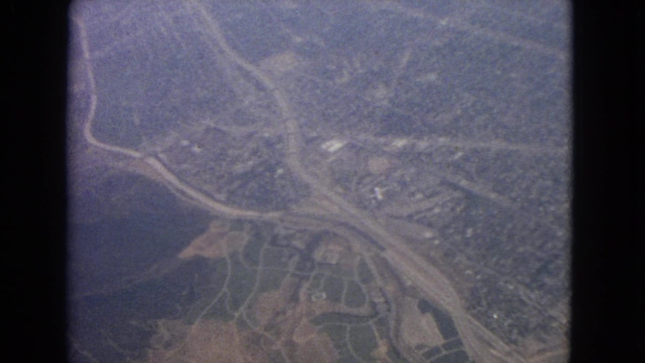 Aerial view of winding roads, fields, and wooded land seen through a dark window frame.