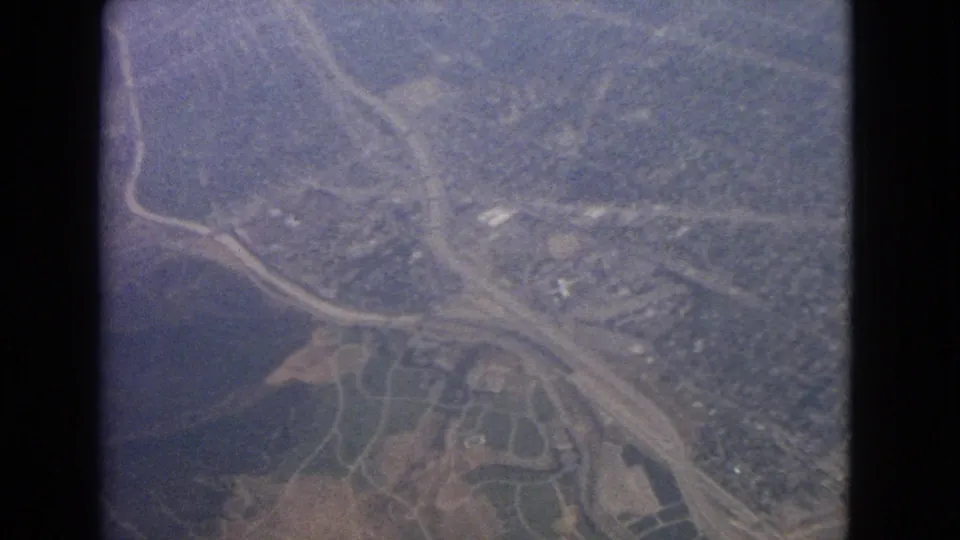 1963 aerial home-movie view likely near Barrington, Illinois, showing roads, fields, wooded terrain, and scattered buildings through a window frame.