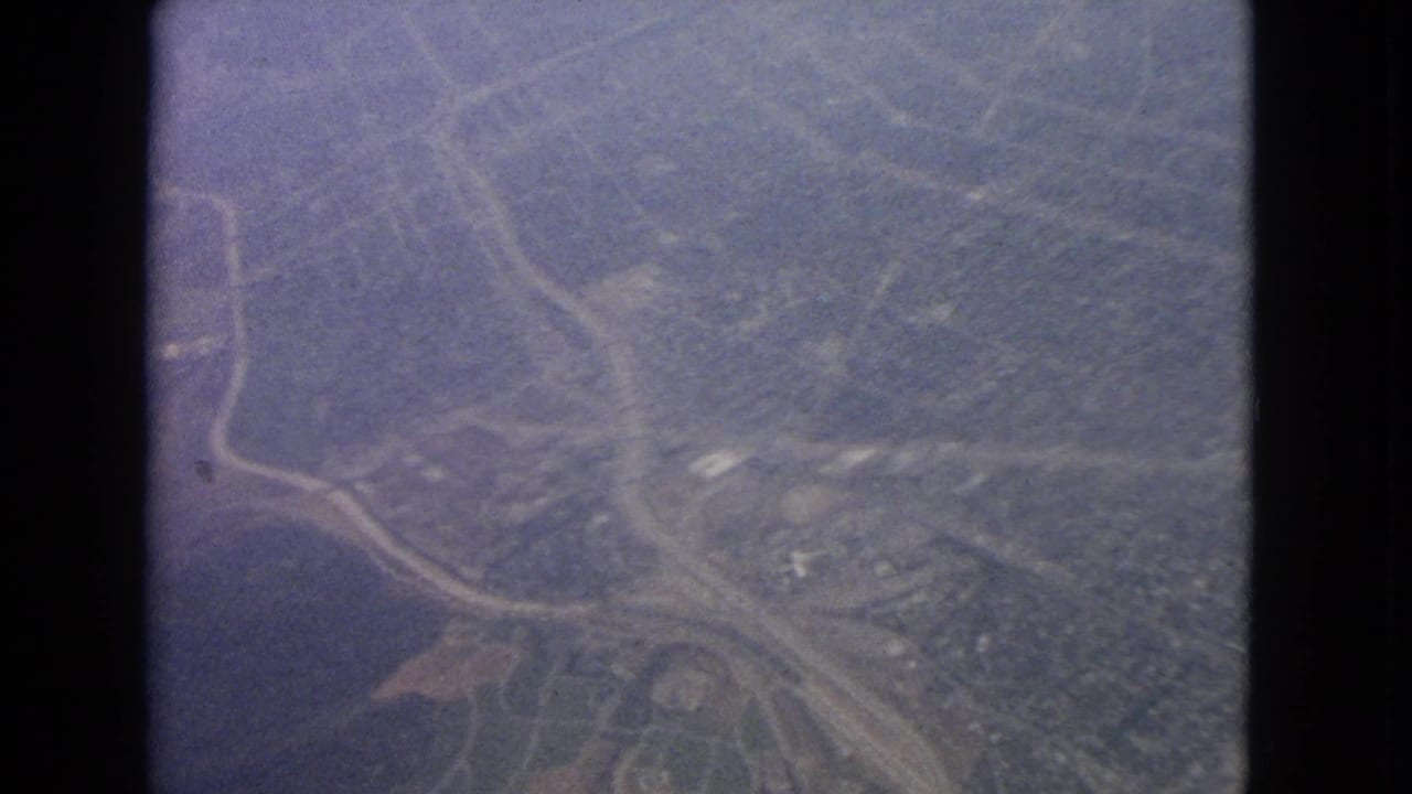 Aerial landscape with roads, wooded hills, and scattered buildings divided by dark film framing.