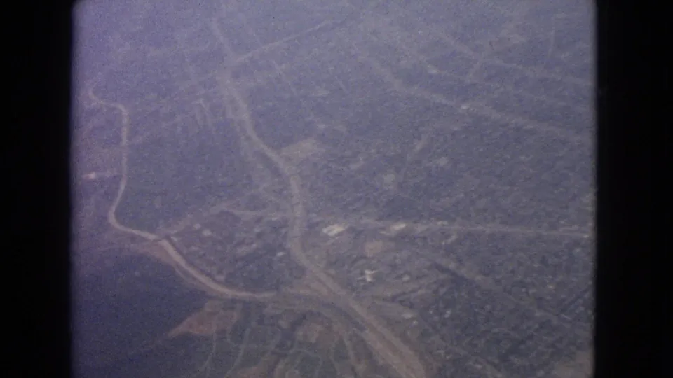 1963 8mm aerial view likely near Barrington, Illinois, showing a road junction, fields, trees, scattered buildings, and a possible shoreline.