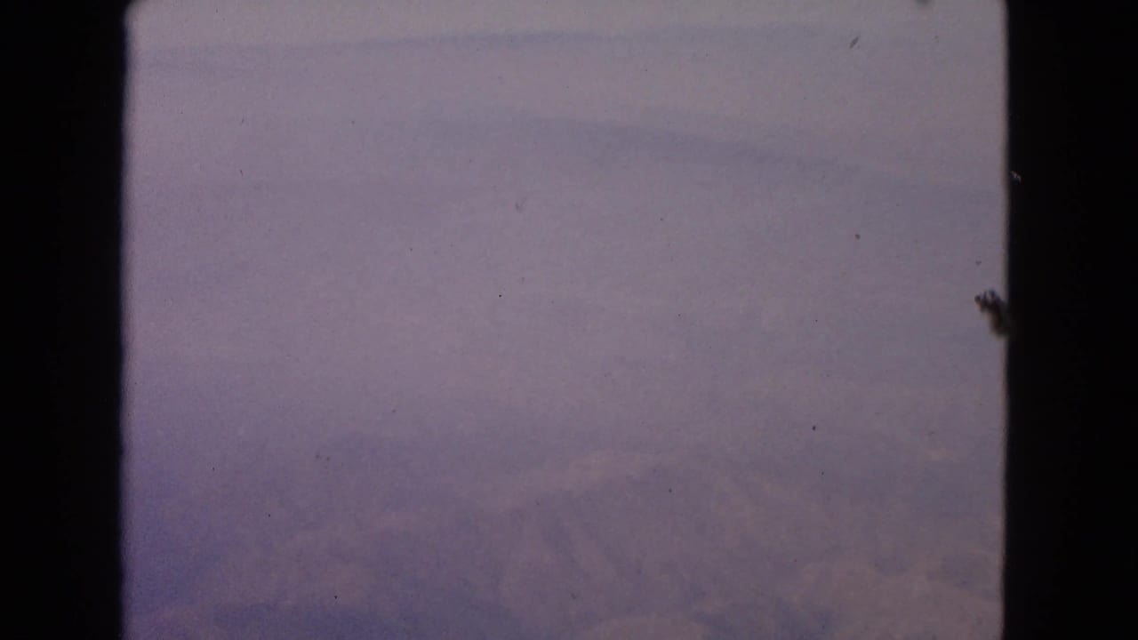Airplane window view with clouds and dark window edges on 8mm film.