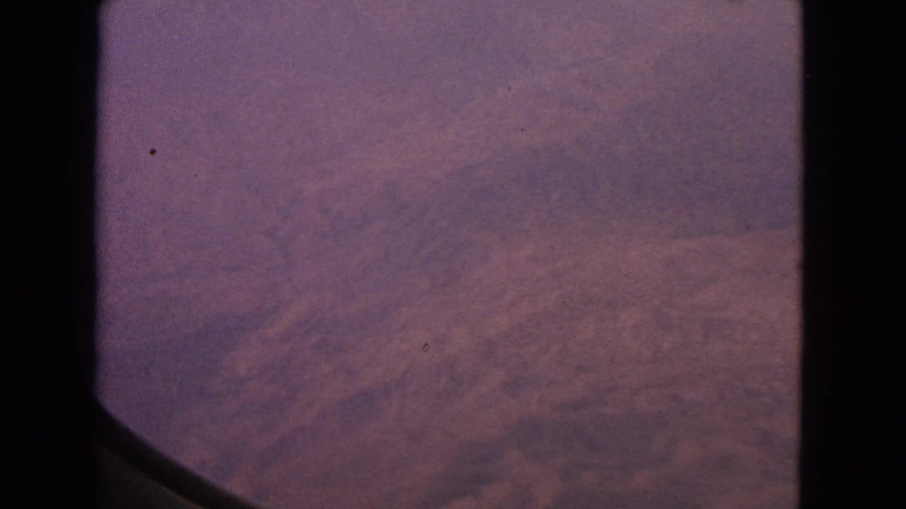 Hazy purple dawn sky seen through a dark airplane window frame.
