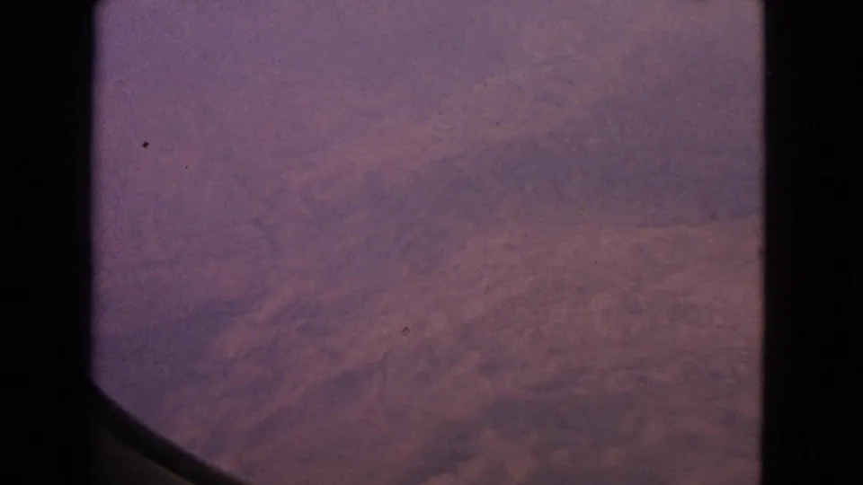 1963 8mm home-movie view from an airplane window, showing hazy purple-pink sky with no visible ground detail.