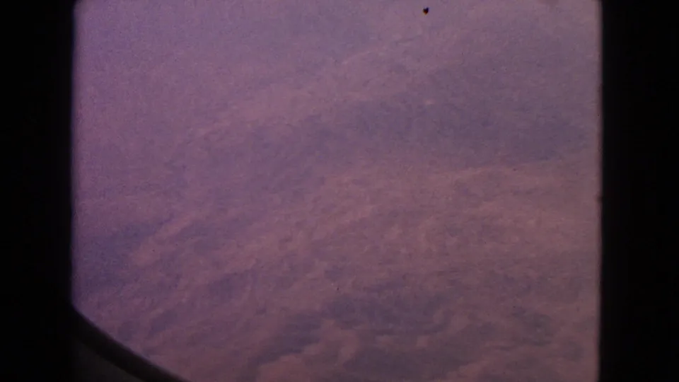 1963 8mm aerial window view with muted purple dawn tones and soft cloud texture, without identifiable landmarks.