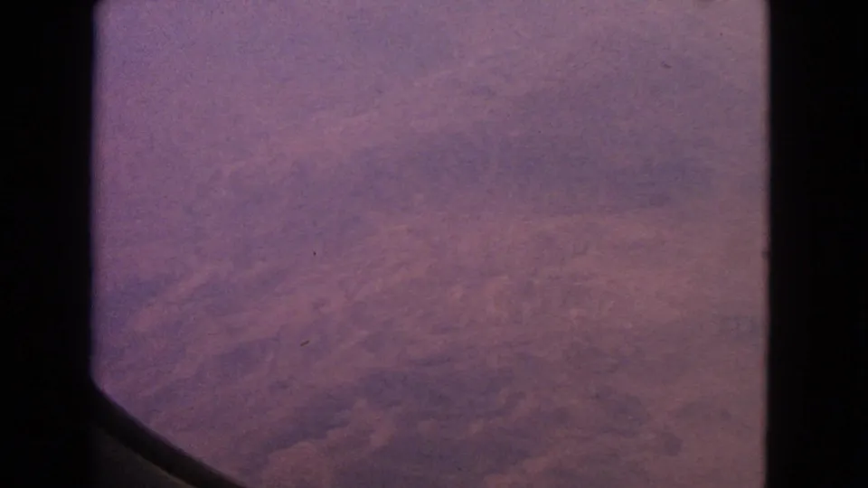 1963 home-movie airplane-window view with hazy dawn color, visible 8mm grain, and no people or landmarks in frame.