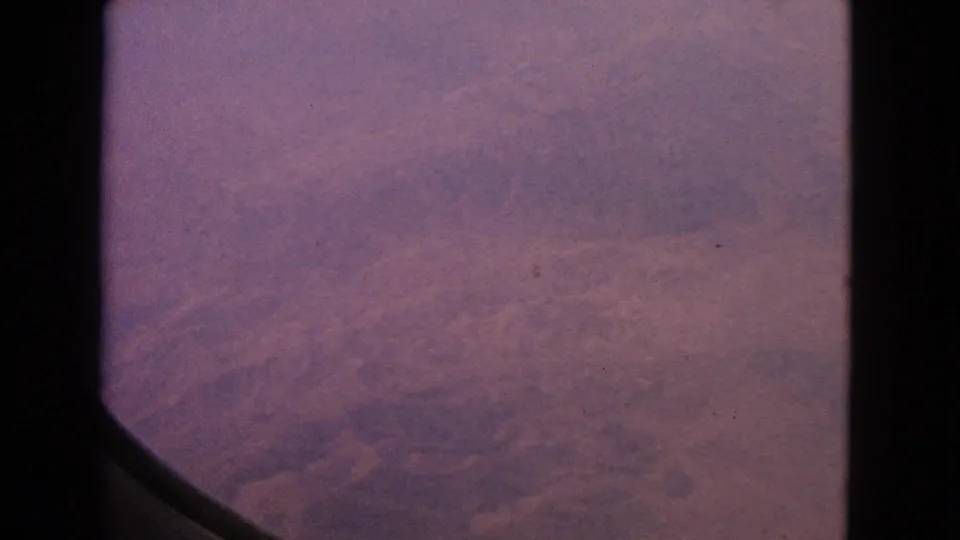 1963 8mm airplane-window shot showing soft purple-pink haze and film texture, with no identifiable ground features.