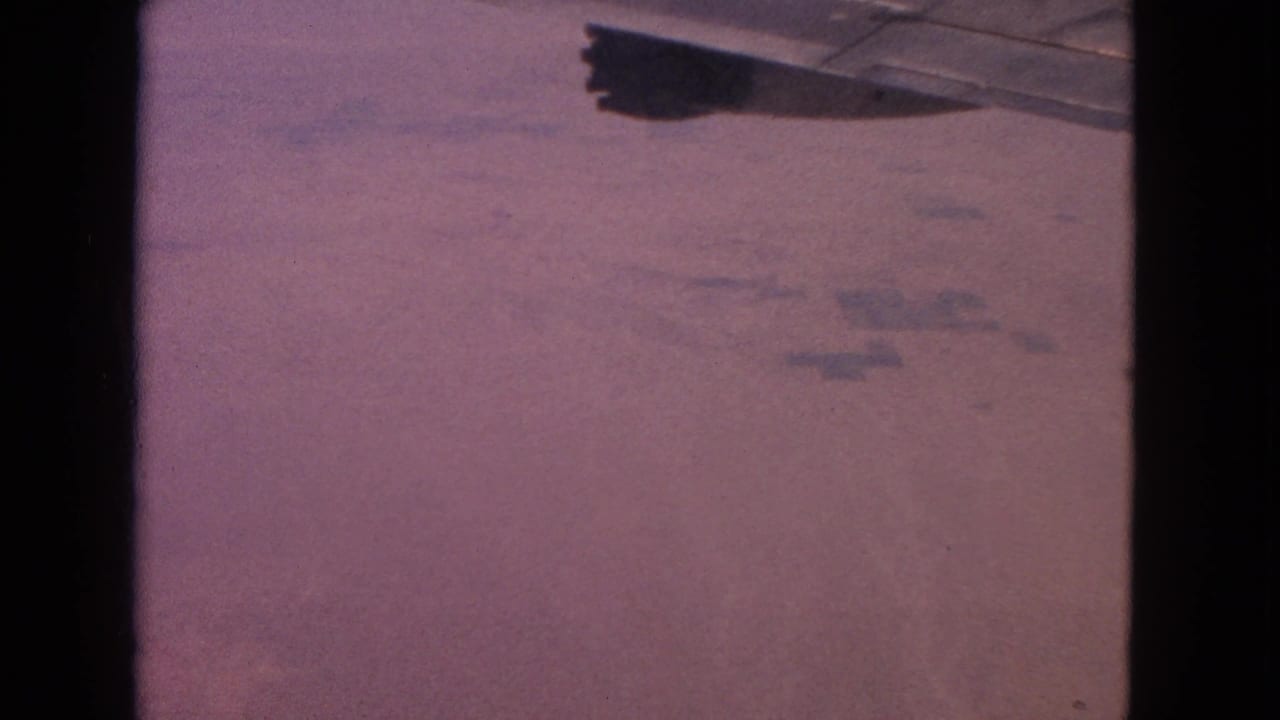 Airplane wing crossing the upper frame over a reddish-purple aerial landscape in 1963 8mm home-movie footage.