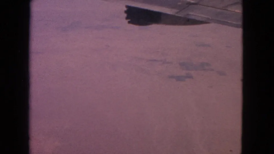 Airplane wing crossing the upper frame over a reddish-purple aerial landscape in 1963 8mm home-movie footage.