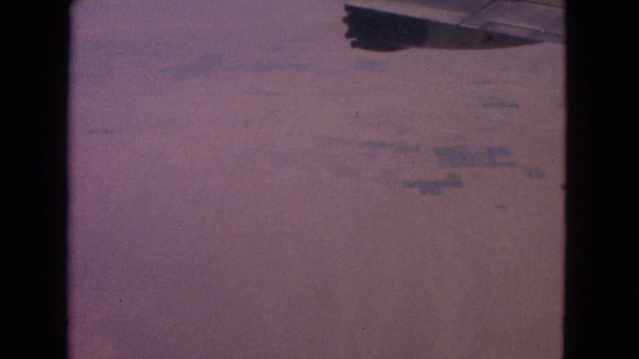 Airplane wing edge above a hazy aerial view of distant ground.