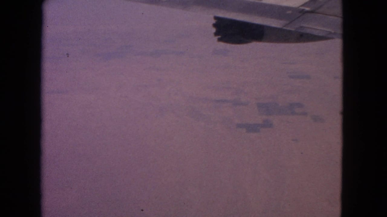 Plane wing at upper right over a soft, hazy view of land below.
