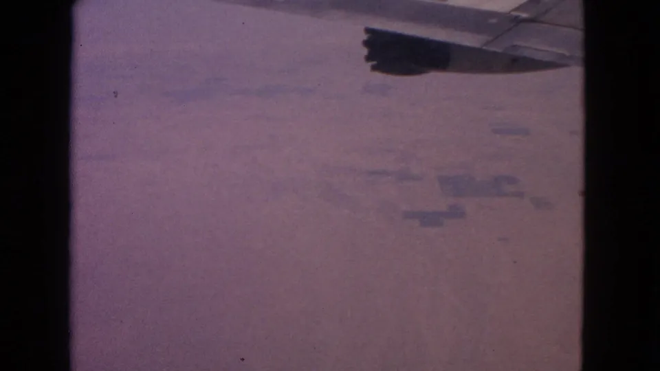 Passenger-window frame from 1963 metadata showing a plane wing over indistinct ground far below.