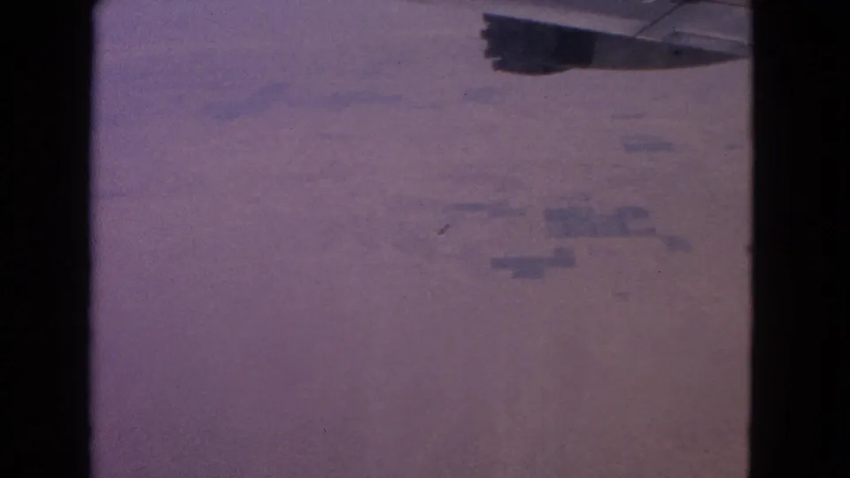 End frame of a 1963 8mm airplane-window view, with wing edge and distant ground softened by haze.