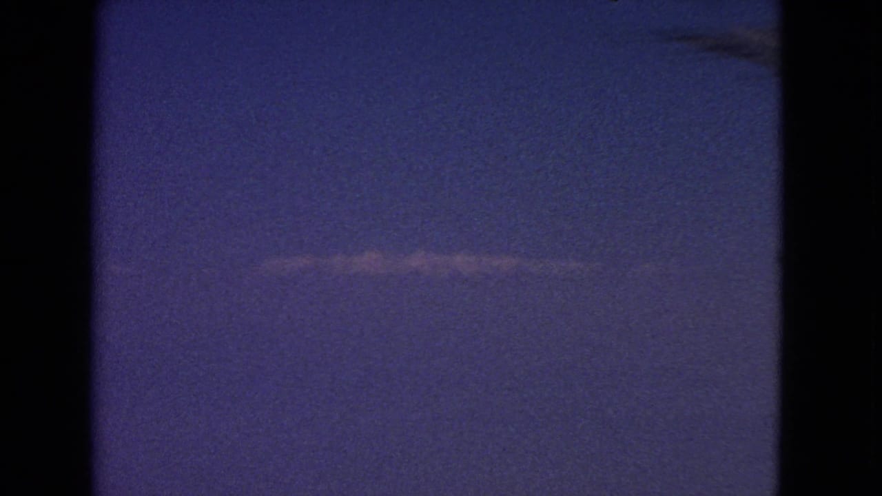 1963 8mm frame showing a thin contrail across a blue-purple sky, with dark window or film-edge borders.